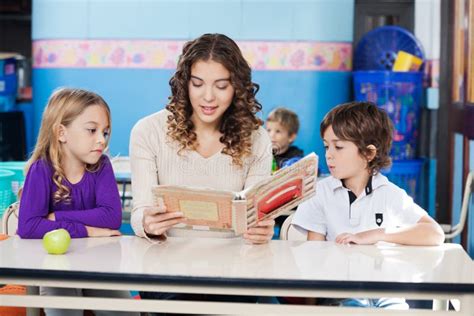 Teacher Reading Book While Children Listening To Stock Photo Image Of