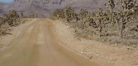 A Dirt Road In The Desert With Mountains In The Background And Trees On