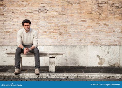Handsome Young Man Sitting On Marble Bench With Bricks Background Stock