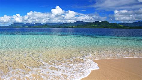 Long View Of Green Covered Mountain With Clear Body Of Water In Ocean