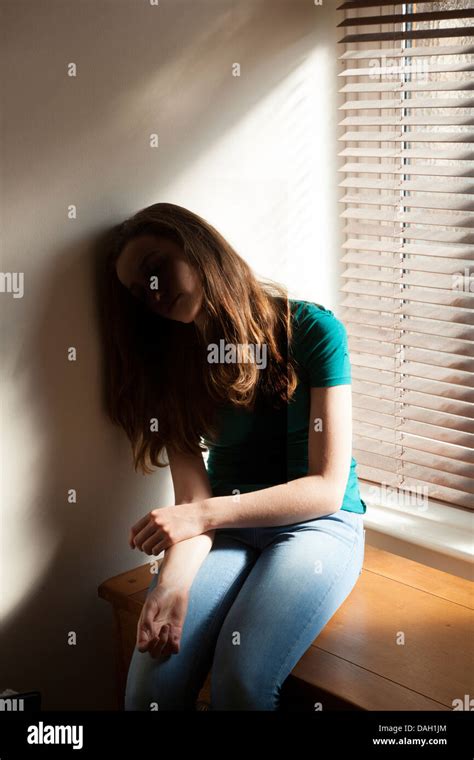A Teenage Girl Sitting Slumped Against The Wall By A Window With Light