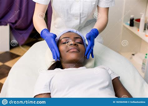 Front View Of Young African Woman Relaxing On Massage Bed Getting Facial Massage At Beauty Spa