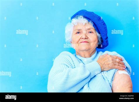 mature woman 80 years old showing her arm with bandage after receiving vaccination in blue
