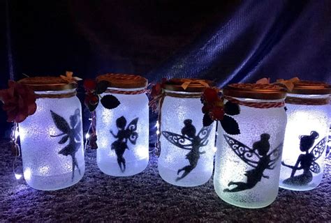 Four Mason Jars With Fairy Lights And Tinkerbells On Them Sitting On A