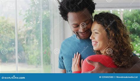 Happy Biracial Couple Embracing Standing At Window And Looking Into Distance Stock Footage