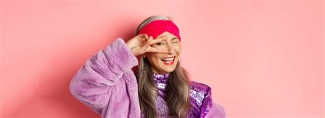 Free Photo Fashion Closeup Of Fashionable Asian Senior Woman Smiling Showing Victory Sign Over