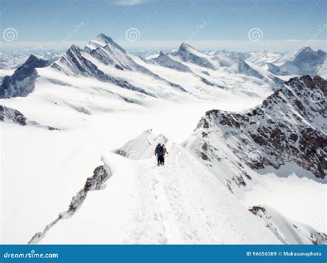 Two Mountain Climbers On A Narrow Ridge In The Swiss Alps With A