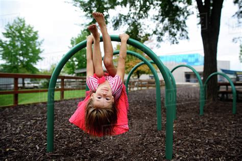 Portrait Of Girl Hanging Upside Down On Outdoor Play Equipment At