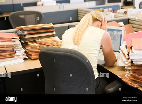 Businesswoman In Cubicle With Laptop And Stacks Of Files Stock Photo