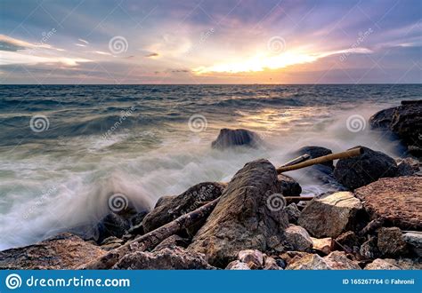 Ocean Water Splash On Rock Beach With Beautiful Sunset Sky And Clouds