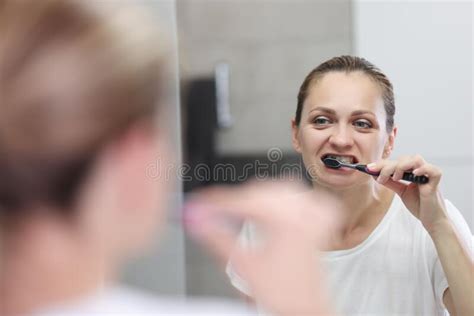Young Woman Brushes Her Teeth In Bathroom In Front Of Mirror Stock