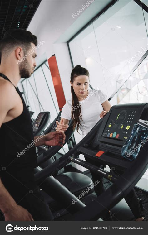 Attractive Trainer Instructing Young Sportsman Standing Treadmill Stock