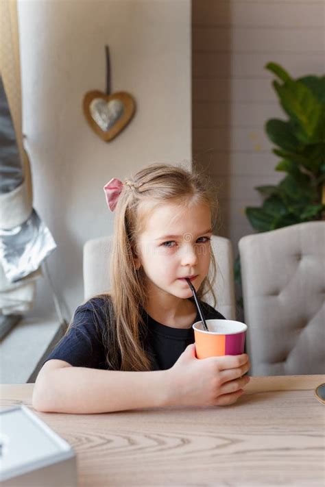 Little Girl Drinking Cacao Through Straw From Paper Cup Sitting At The