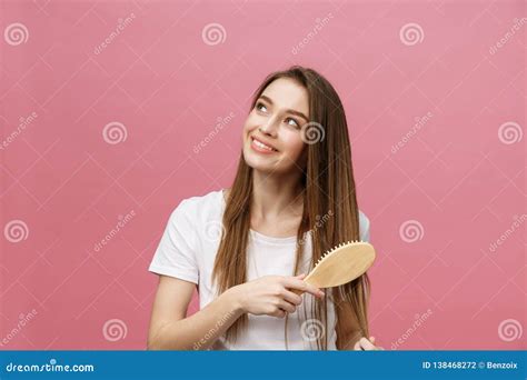 Smiling Young Woman Combing Hair And Looking Away Isolated On Pink