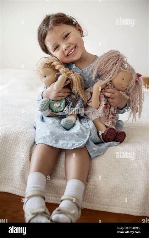 Cute Little Girl With Blond Hair Holding Her Dolls And Smiling Stock