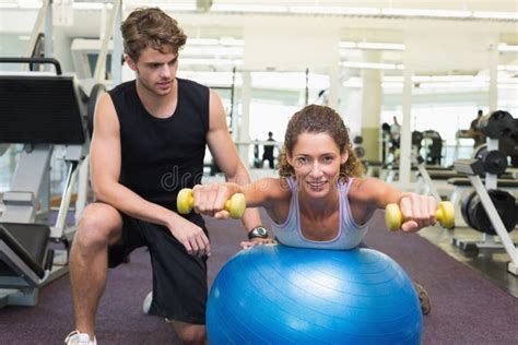 Trainer Watching Client Balance On Exercise Ball With Dumbbells Stock