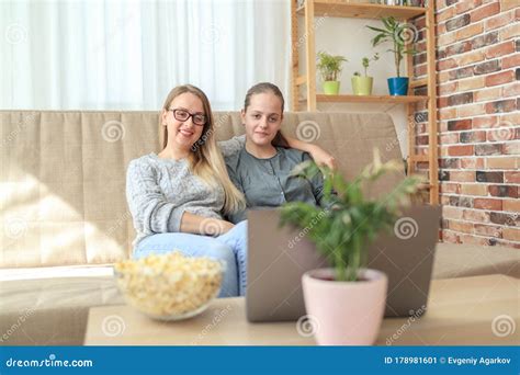 Mother And Daughter Sitting On Sofa In Living Room Together And Looking Learning Course Stock
