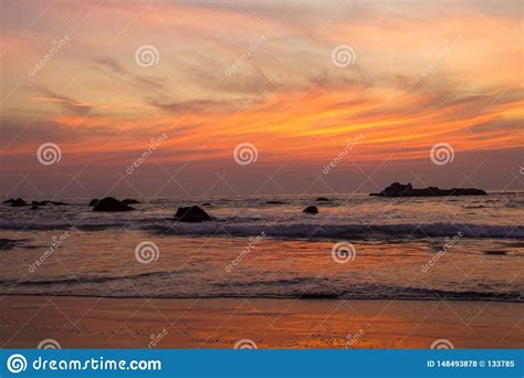 Sandy Beach On A Background Of Sea Waves With Rocks Under Bright Orange