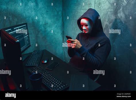 Anonymous Hacker Wearing Face Mask Working On Computer In Dark Room
