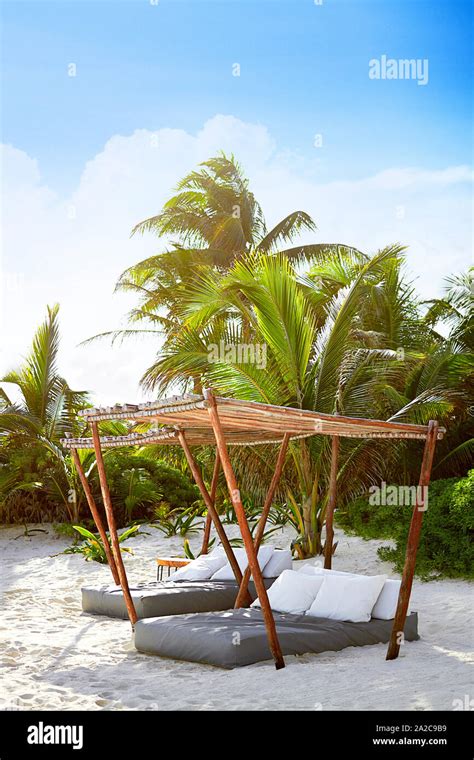 Lounge Beds Shaded Under Canopies On White Sandy Beach With Palm Trees In Background Stock Photo