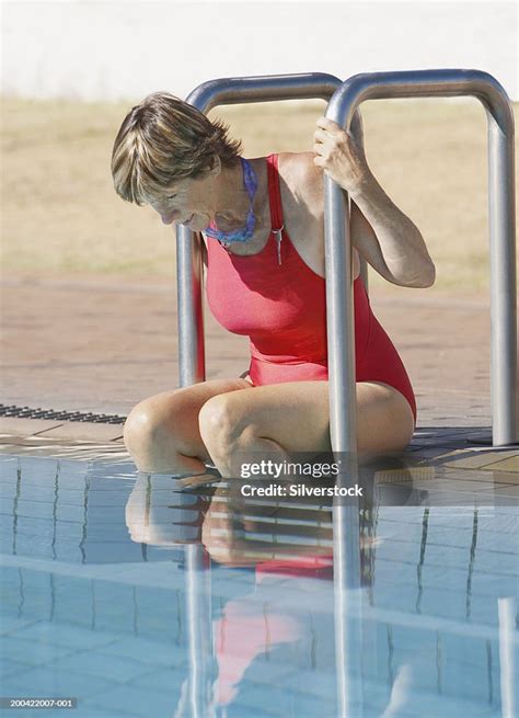 Mature Woman Sitting At Edge Of Swimming Pool Wearing Swimsuit Stock
