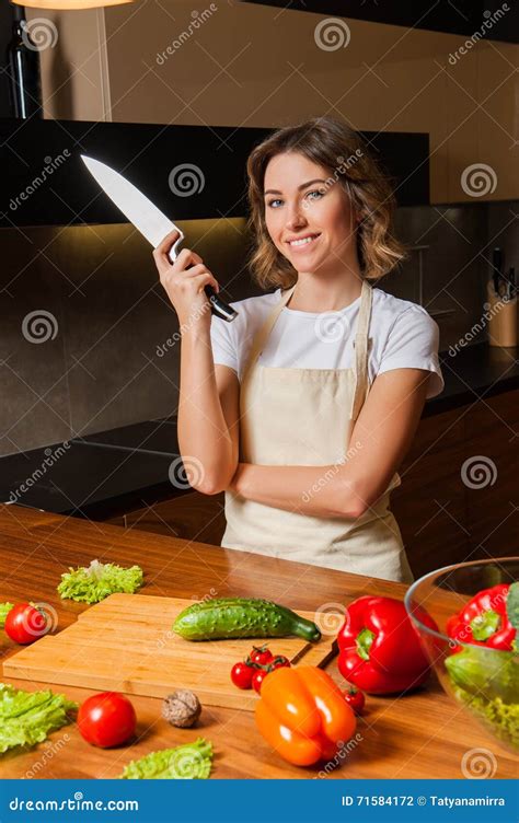 Pretty Woman In Kitchen With Knife Looking To The Camera Stock Photo