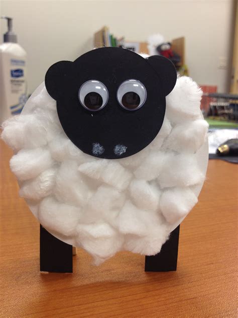 A Black And White Sheep With Big Eyes On Its Head Sitting On A Wooden