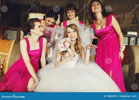 bride lloks funny while bridesmaids in pink dresses hold her veil stock image image of