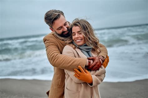 Premium Photo Beautiful Married Couple Hugging On The Seashore Wearing A Coat In Winter