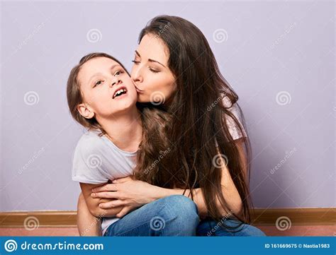 Happy Excited Mother Cuddling And Kissing Her Daughter On Purple Background With Empty Copy