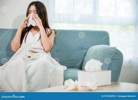 Sick Female Sitting Under Blanket On Sofa And Sneeze With Tissue Paper