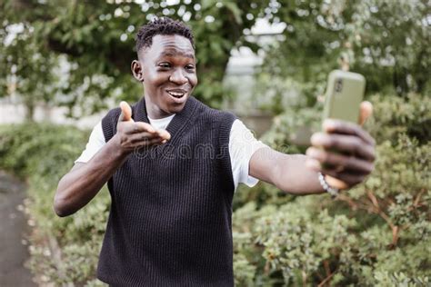 Young African Man Taking Selfie Or Vlogging On Phone In Park Smiling