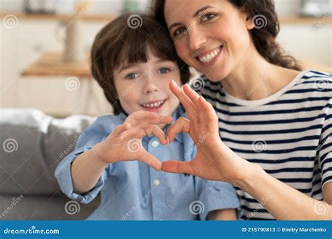 mom and son make heart hand gesture together happy smiling look in camera at home sitting on