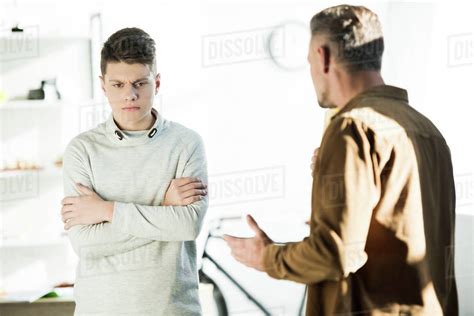 Irritated Father Gesturing And Looking At Teen Son With Crossed Arms At