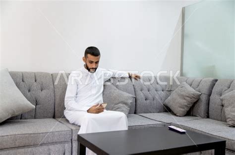 رجل سعودي خليجي جالس ينتظر دوره في صالون الحلاقة ، يقضي وقته على هاتفه المحمول ، العناية