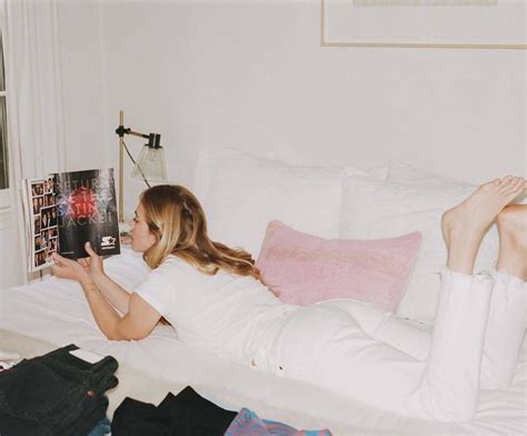 A Woman Laying On Top Of A White Bed Next To A Book And Some Clothes