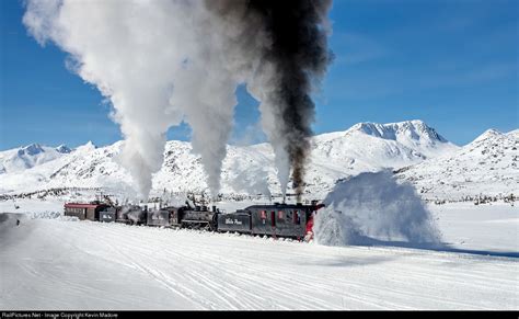 A Train Traveling Through Snow Covered Mountains With Steam Pouring Out