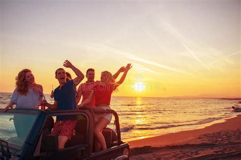 Young People Having Fun In Convertible Car At The Beach At Sunset