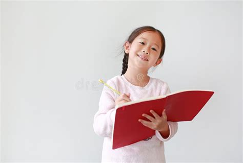 Happy Little Asian Child Girl Writes In A Book Or Notebook With Pencil