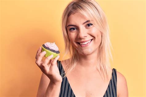 Young Beautiful Blonde Woman Eating Sweet Chocolate Cupcake Over
