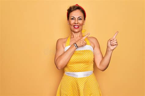 middle age senior pin up woman wearing 50s style retro dress over yellow background smiling and