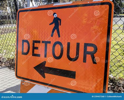 Angled View Of An Orange Detour Sign On A Sidewalk Near A Construction