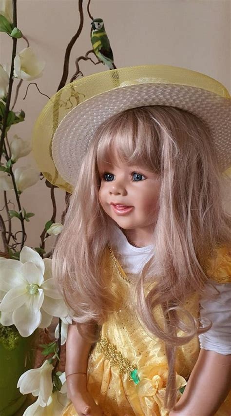 A Doll With Blonde Hair Wearing A Yellow Dress And Hat Sitting In Front