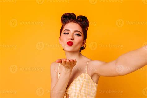 sensual pretty woman sending air kiss lovely pinup girl taking selfie on yellow background