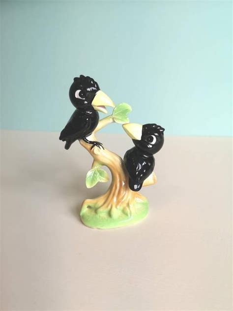 Two Black Birds Sitting On Top Of A Tree Branch With Leaves In Their Beaks
