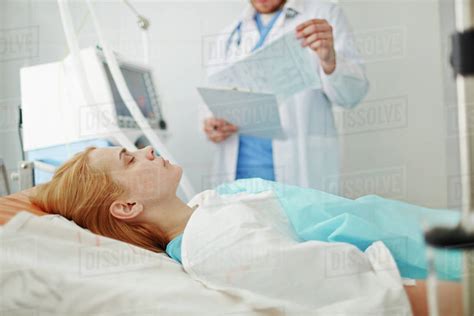Unconscious Woman Lying On Bed In Hospital With Doctor Standing Nearby
