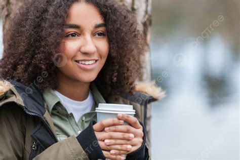 美しい幸せな混血の異人種間のアフリカ系アメリカ人の女の子 10 代の女性の若い女性が笑顔で外の湖のそばでテイクアウトのコーヒーを飲みながら