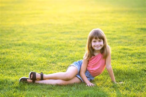 Young Pretty Child Girl Laying Down On Green Grass Lawn On Warm Summer