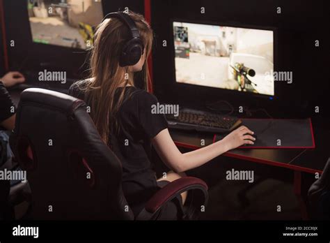 Rear View Of Female Gamer Girl With Headset Sits In A Dark Room Behind