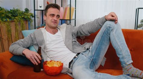 Man Sitting On Sofa Eating Chips And Watching Interesting TV Serial